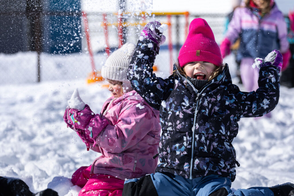 Photo d'un groupe d'enfants du CPE Flocon de rêve, à l'extérieur en hiver, souriant et jouant avec la neige
