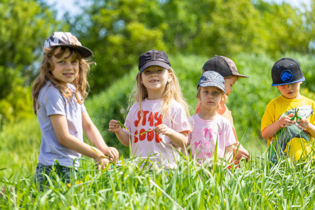Photo d'un groupe d'enfants du CPE Flocon de rêve, à l'extérieur en été, jouant dans un champ d'herbes hautes