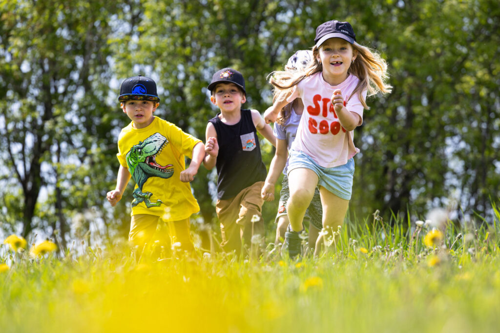Photo d'un groupe d'enfants du CPE Flocon de rêve, à l'extérieur en été, courant dans un champ de pissenlits