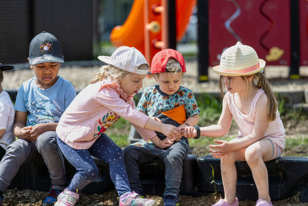 Photo d'un groupe d'enfants du CPE Flocon de rêve, s'échangeant des objets dans une aire de jeu à l'extérieur en été