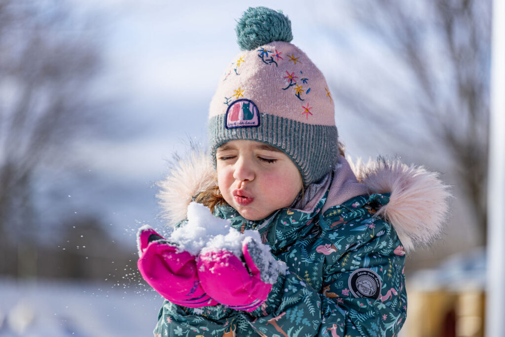Photo d'une petite fille du CPE Flocon de rêve, soufflant de la neige entre ses mains, dehors en hiver